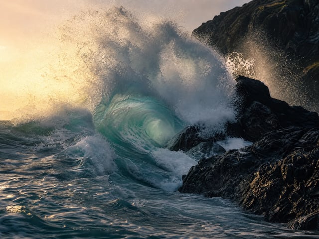 Ocean wave crashing on dark rocks, evoking motion and sound in one pass